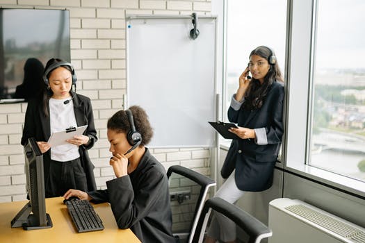 Three women in black blazers with headsets working as customer support agents