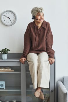 Positive black woman in headset sitting on cupboard 