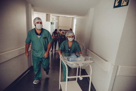 Unrecognizable obstetrician and nurse carrying newborn baby trolley in hospital 