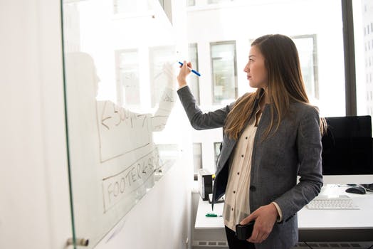 Woman wearing gray blazer writing on dry erase board