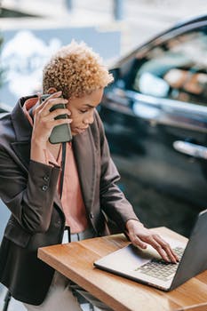 Black businesswoman speaking on smartphone and typing on laptop