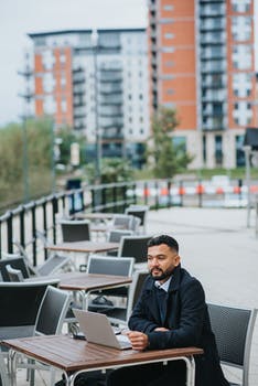 Thoughtful ethnic entrepreneur with laptop in street cafe