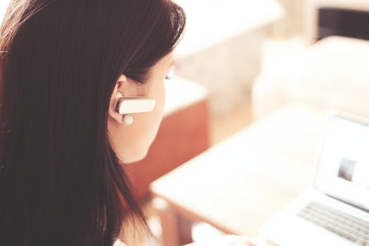 Woman wearing earpiece using white laptop computer