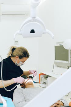 Female dentist treating teeth of male client in clinic