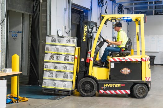 Man riding a yellow forklift lifting boxes