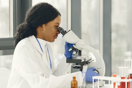 Woman wearing a white lab coat looking through a microscope