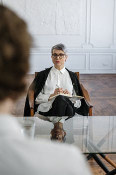 Woman in black blazer and white dress sitting on chair