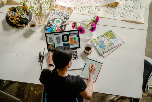 Photo of woman writing on tablet computer while using laptop