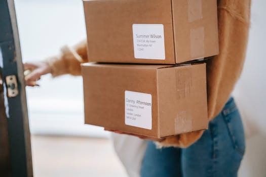 Crop unrecognizable woman carrying boxes and entering post office