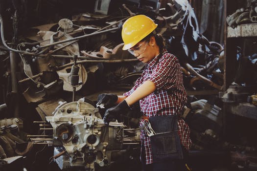 Woman wears yellow hard hat holding vehicle part