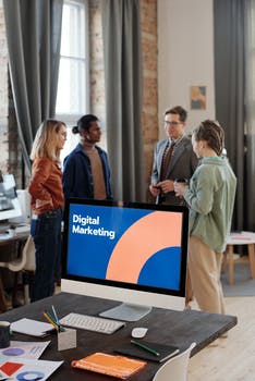 A group of people standing near a computer on the table