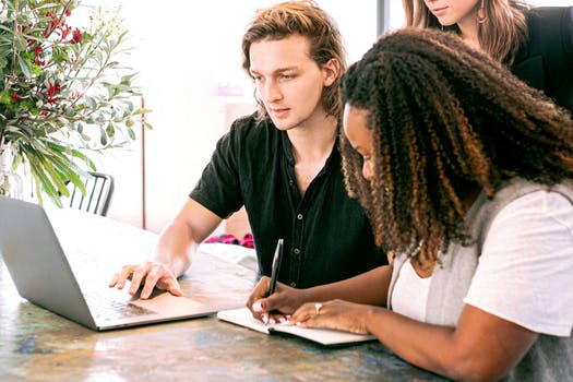 Man working on laptop while woman takes notes