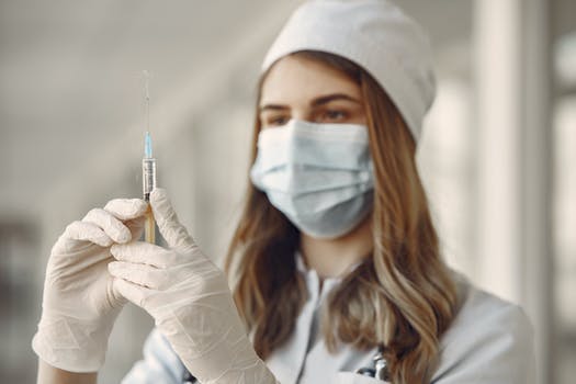 Woman in white long sleeve shirt wearing white face mask holding injection