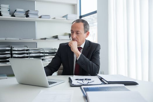 Pensive man sitting behind his desk using laptop