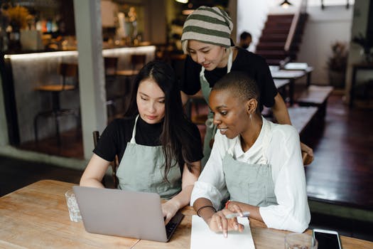 Positive young colleagues in aprons working on laptop in cafe