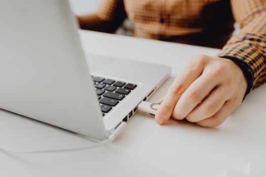 Photo of a person s hand plugging in a flash drive into a laptop